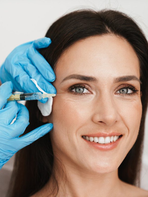 Photo of smiling woman getting mesotherapy treatment in face by specialist in gloves in beauty salon